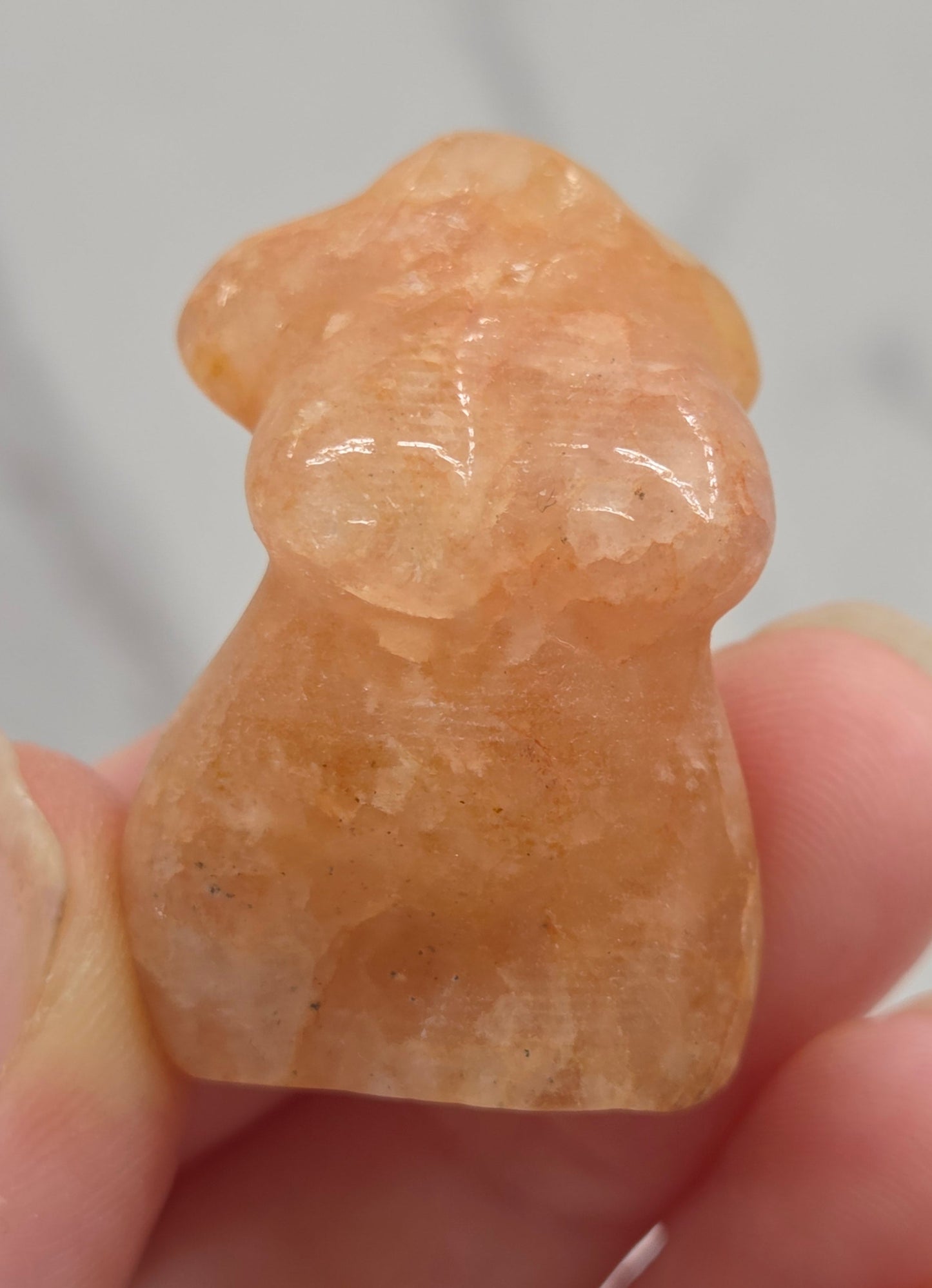 Hand holding a small crystal carving of a female torso against a white background