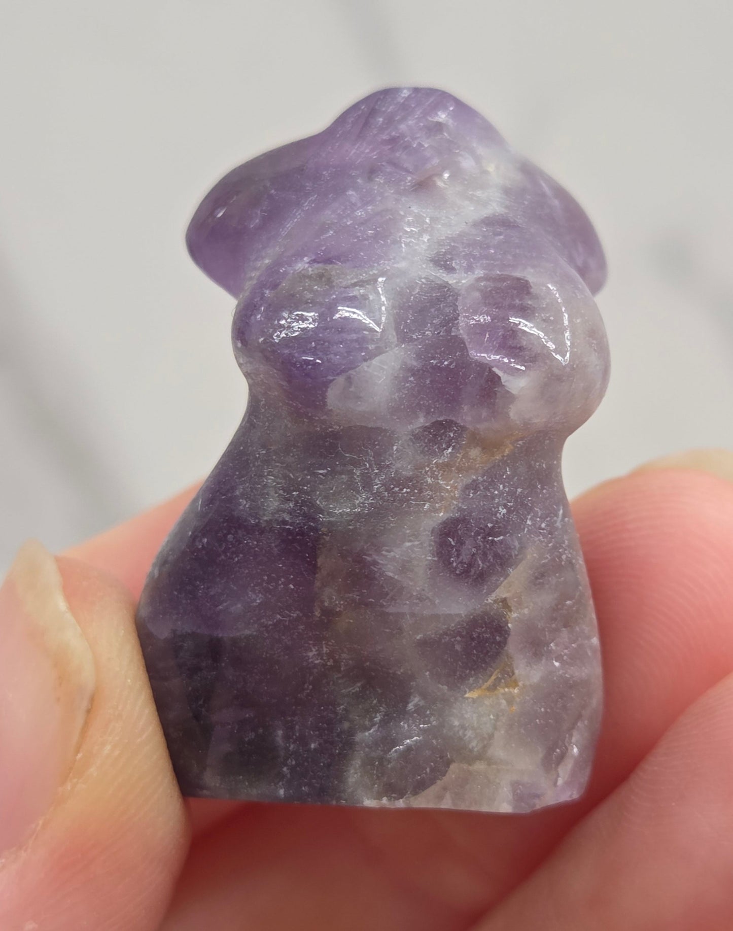 Hand holding a small crystal carving of a female torso against a white background