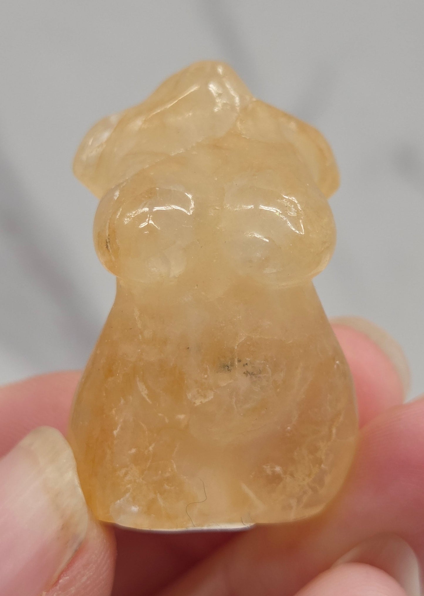 Hand holding a small crystal carving of a female torso against a white background