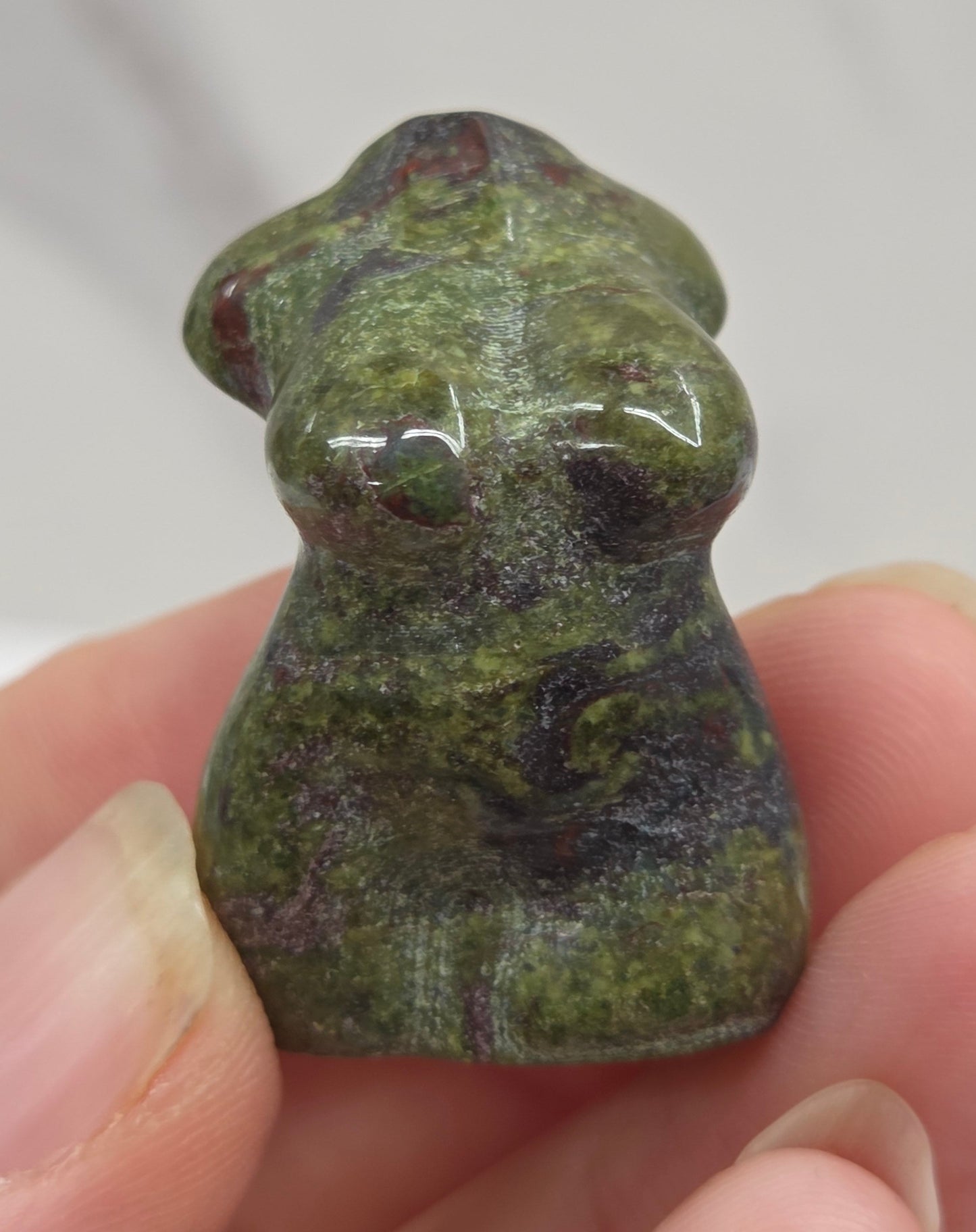 Hand holding a small crystal carving of a female torso against a white background