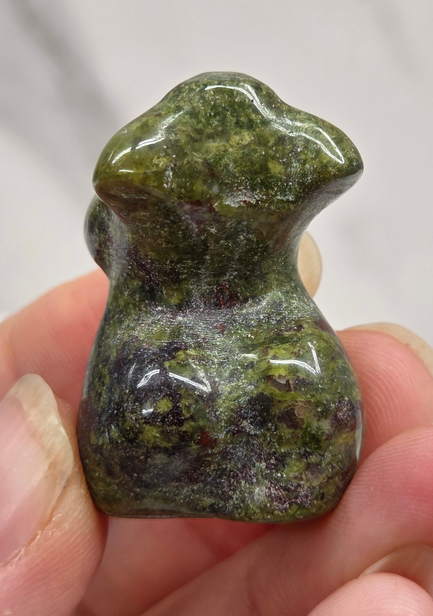Hand holding a small crystal carving of a female torso against a white background