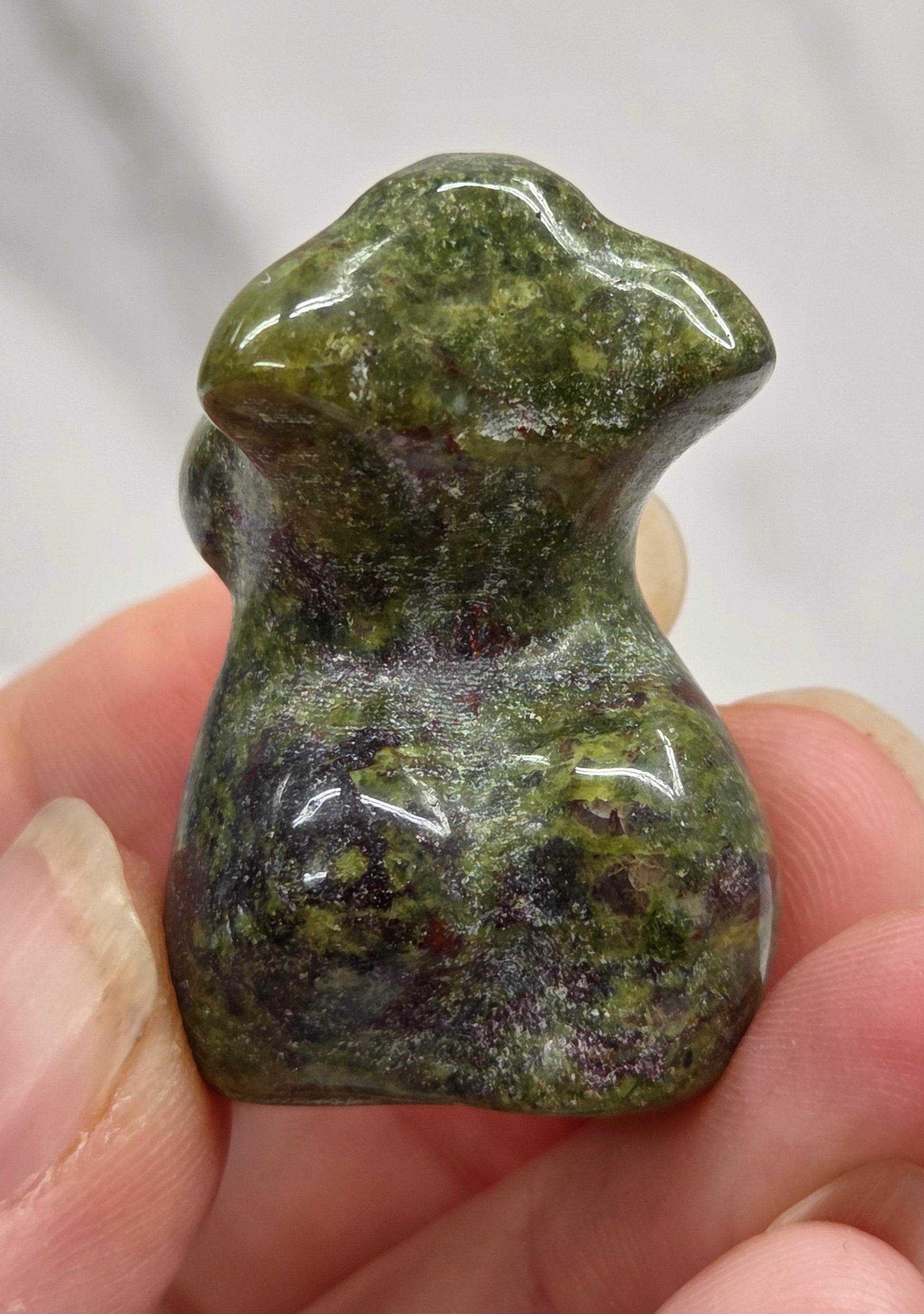 Hand holding a small crystal carving of a female torso against a white background