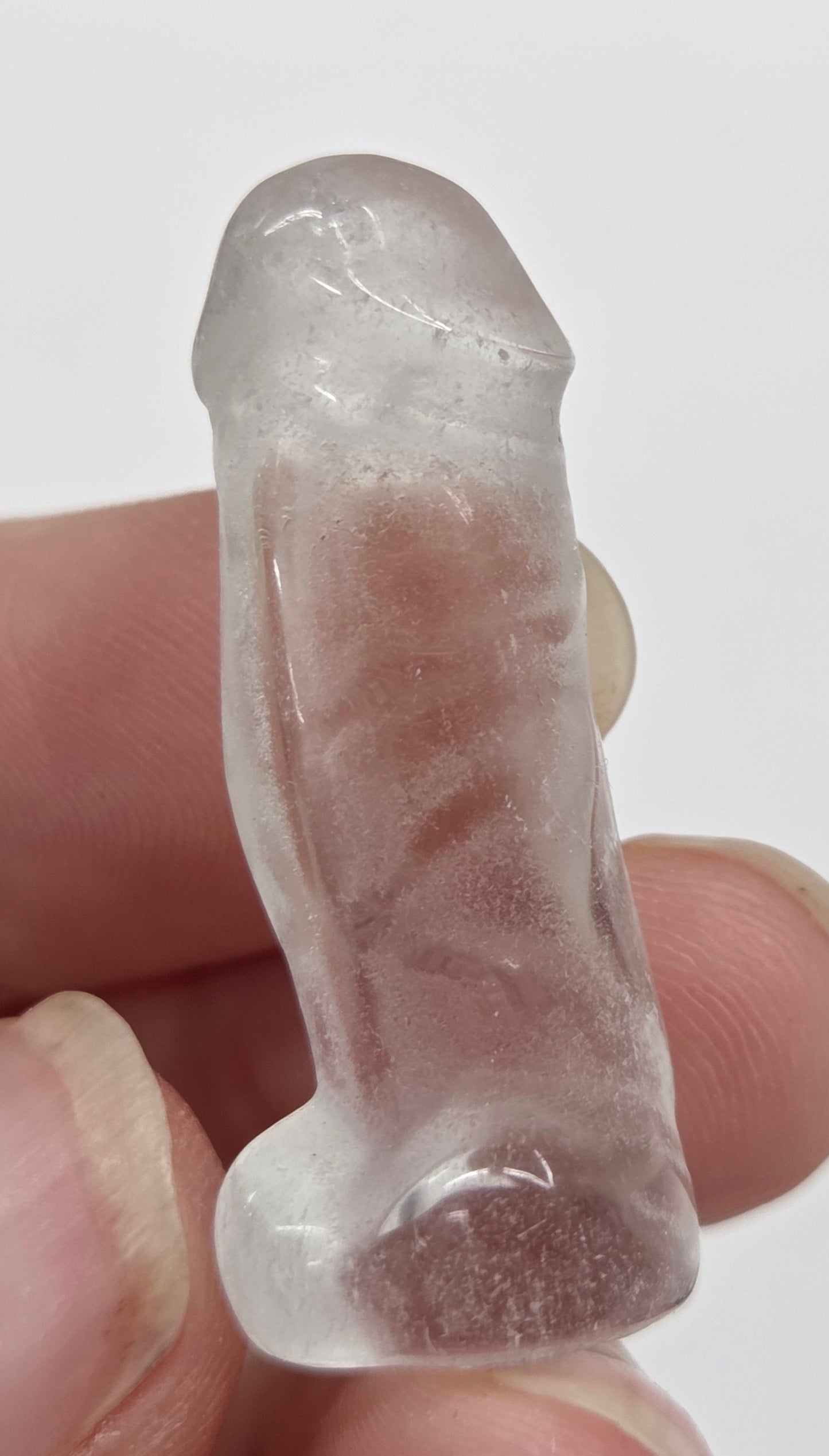 Hand holding a male anatomy crystal carving on a white background