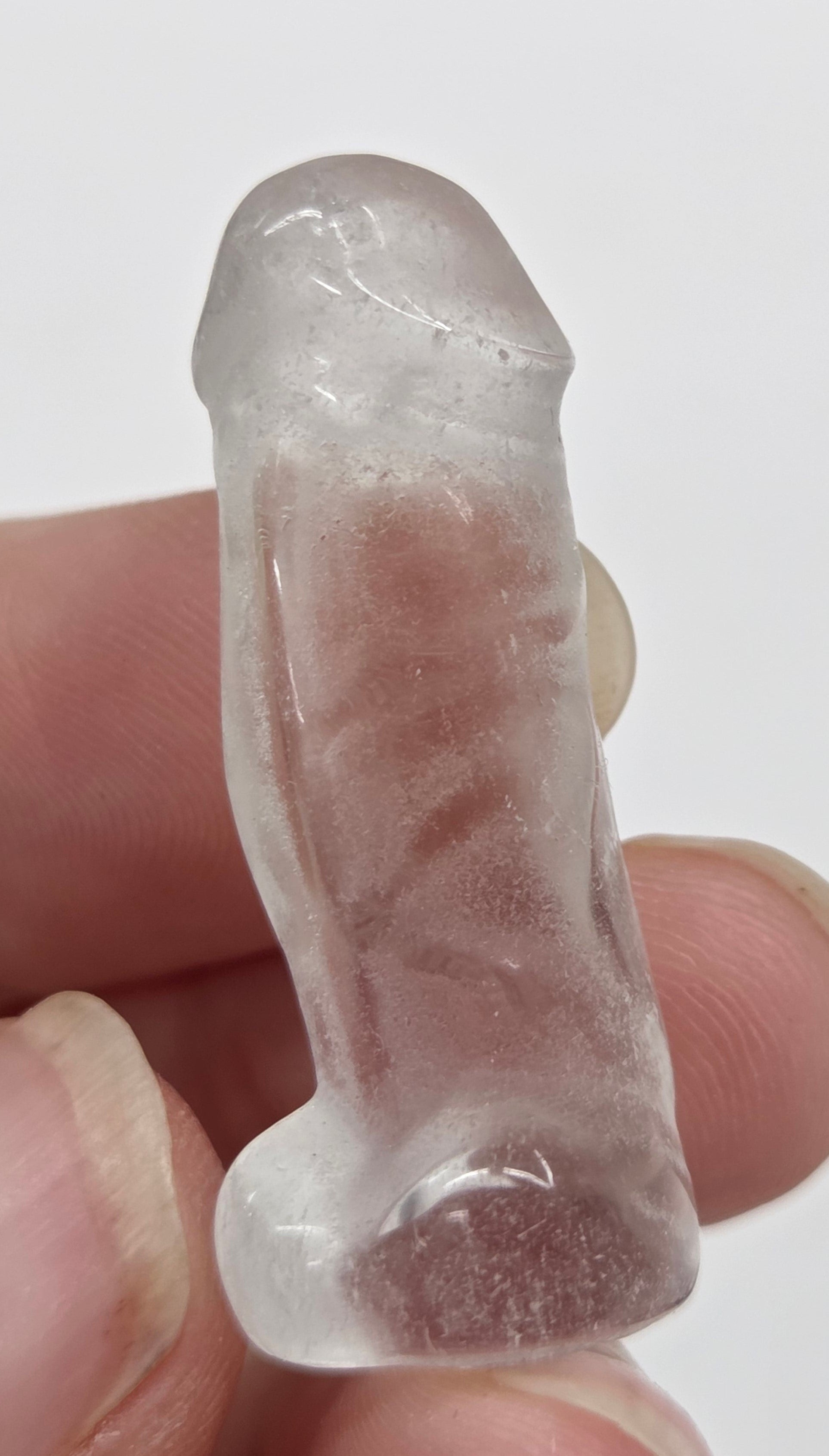 Hand holding a male anatomy crystal carving on a white background