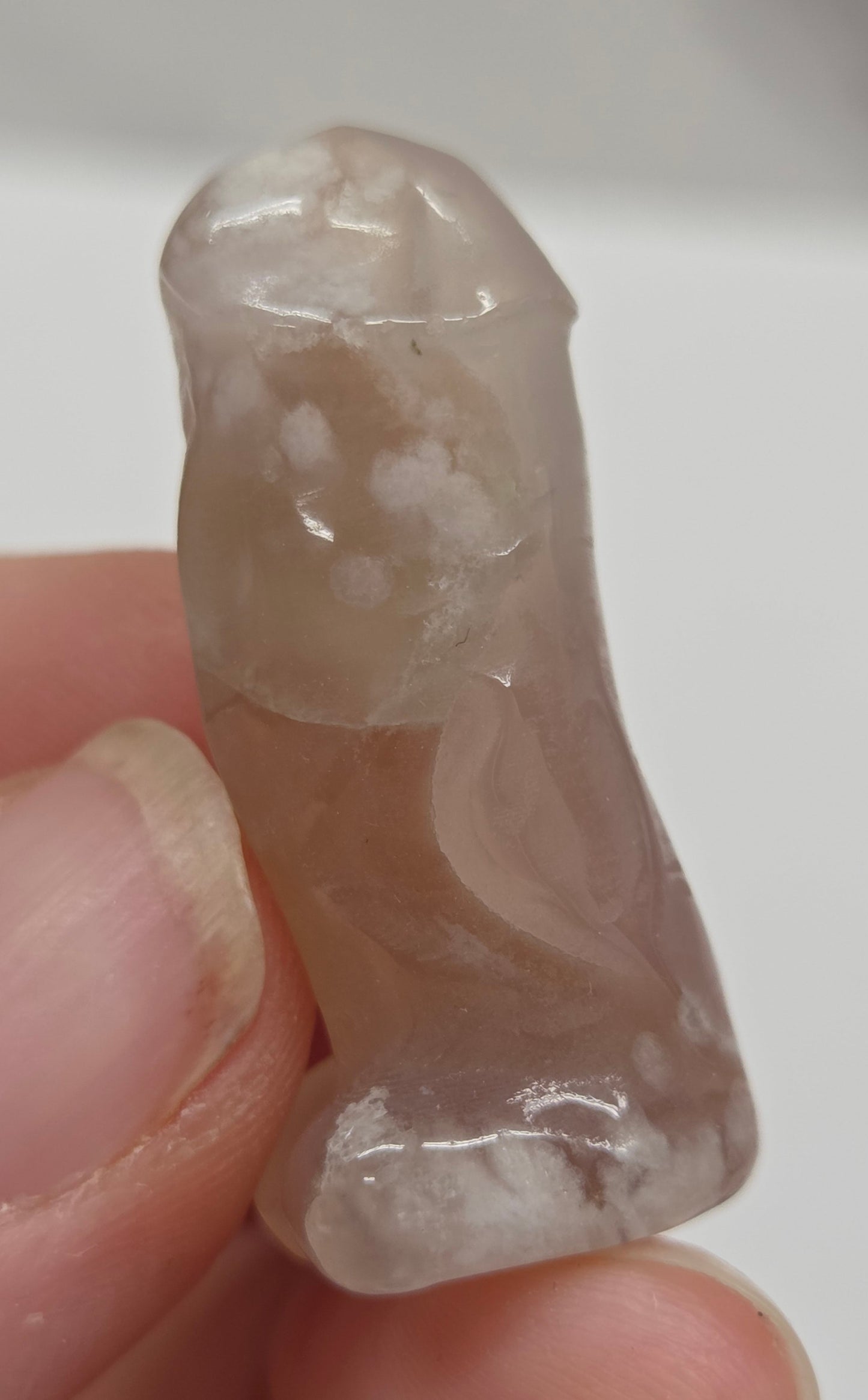Hand holding a male anatomy crystal carving on a white background