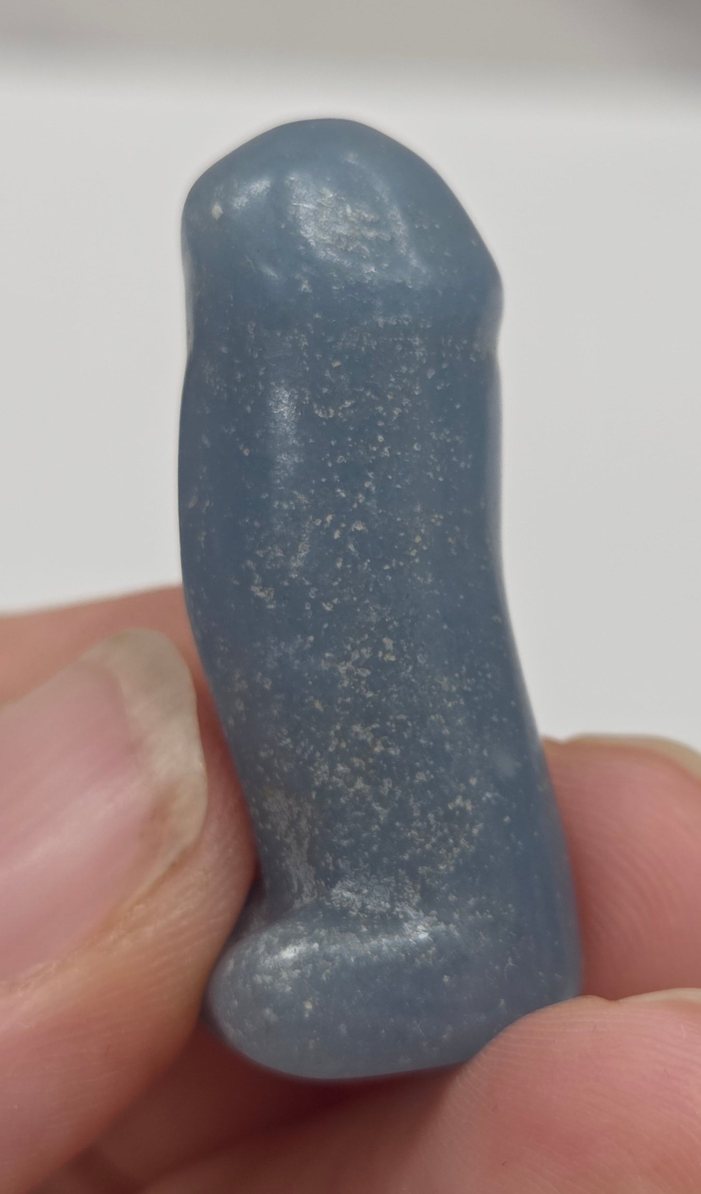 Hand holding a male anatomy crystal carving on a white background