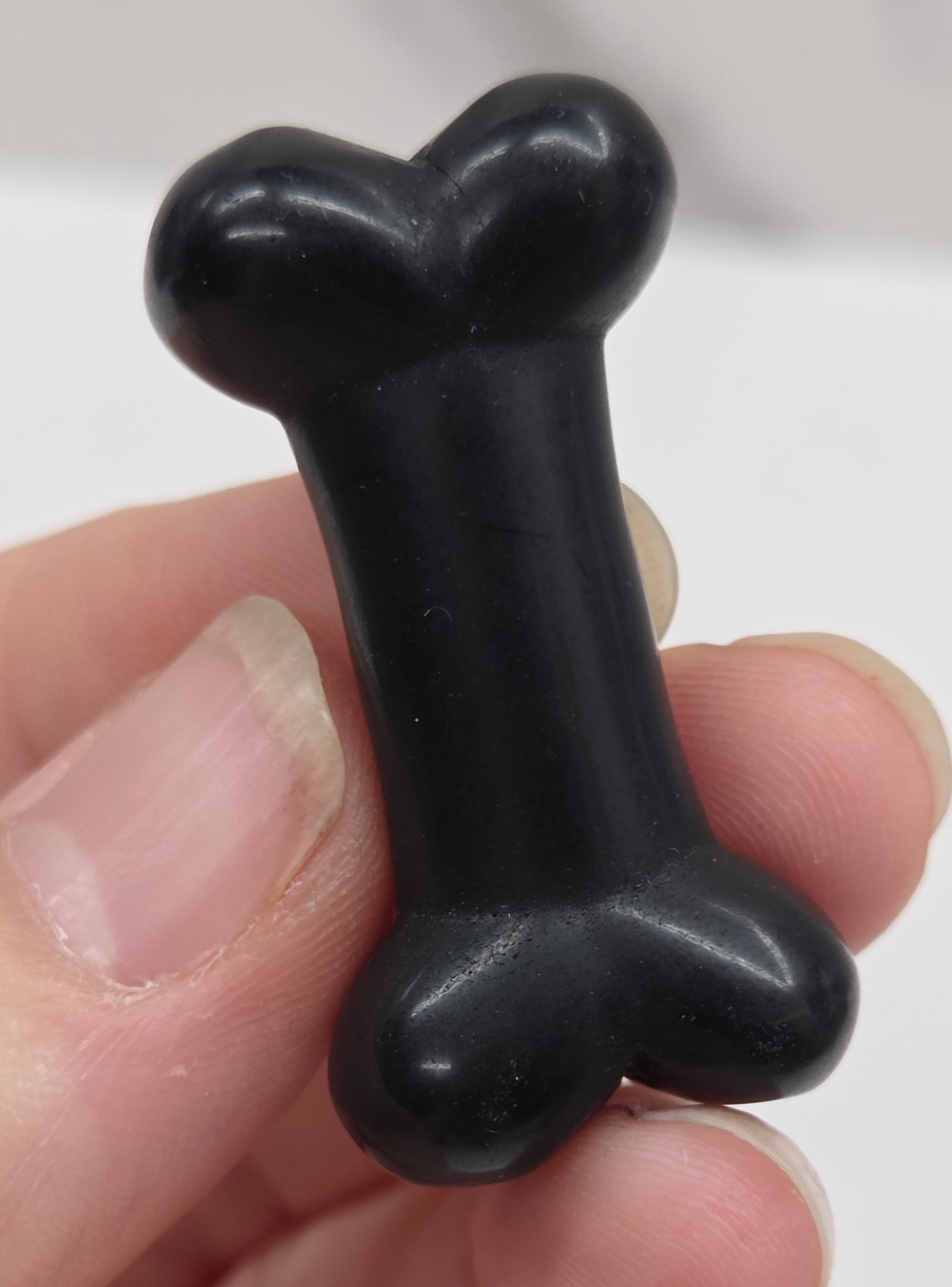 Obsidian carving of a bone being held in a hand on a white backgroung