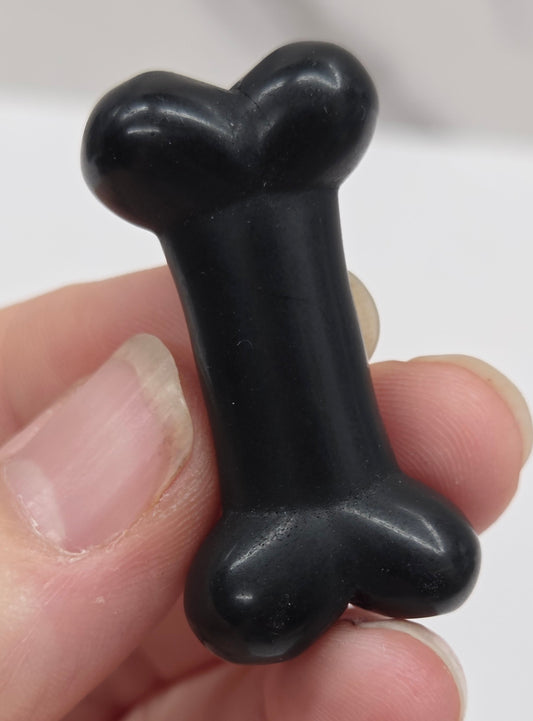 Obsidian carving of a bone being held in a hand on a white backgroung