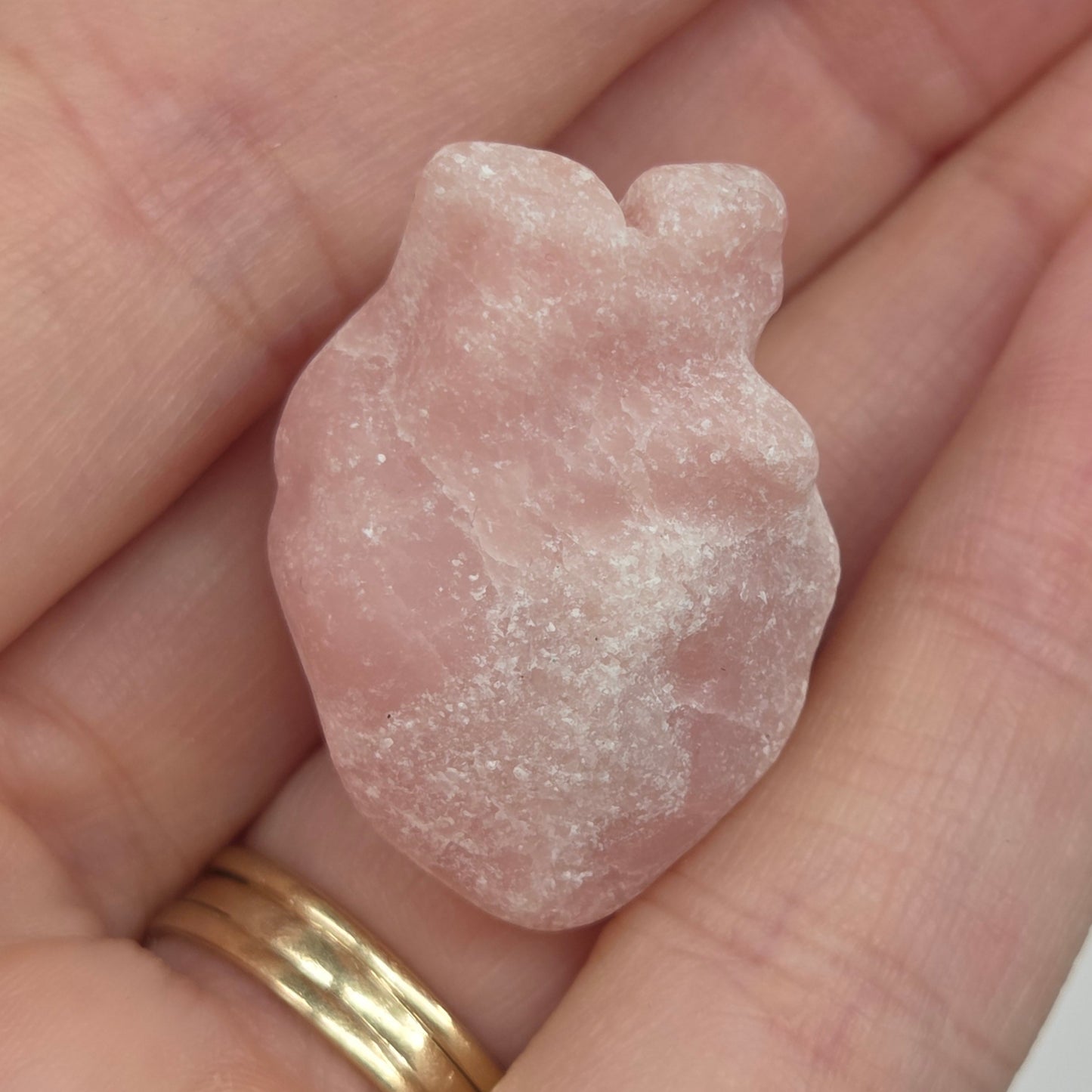 Hand holding a Pink Opal heart shaped carving on a white background