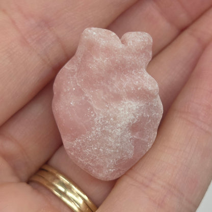 Hand holding a Pink Opal heart shaped carving on a white background