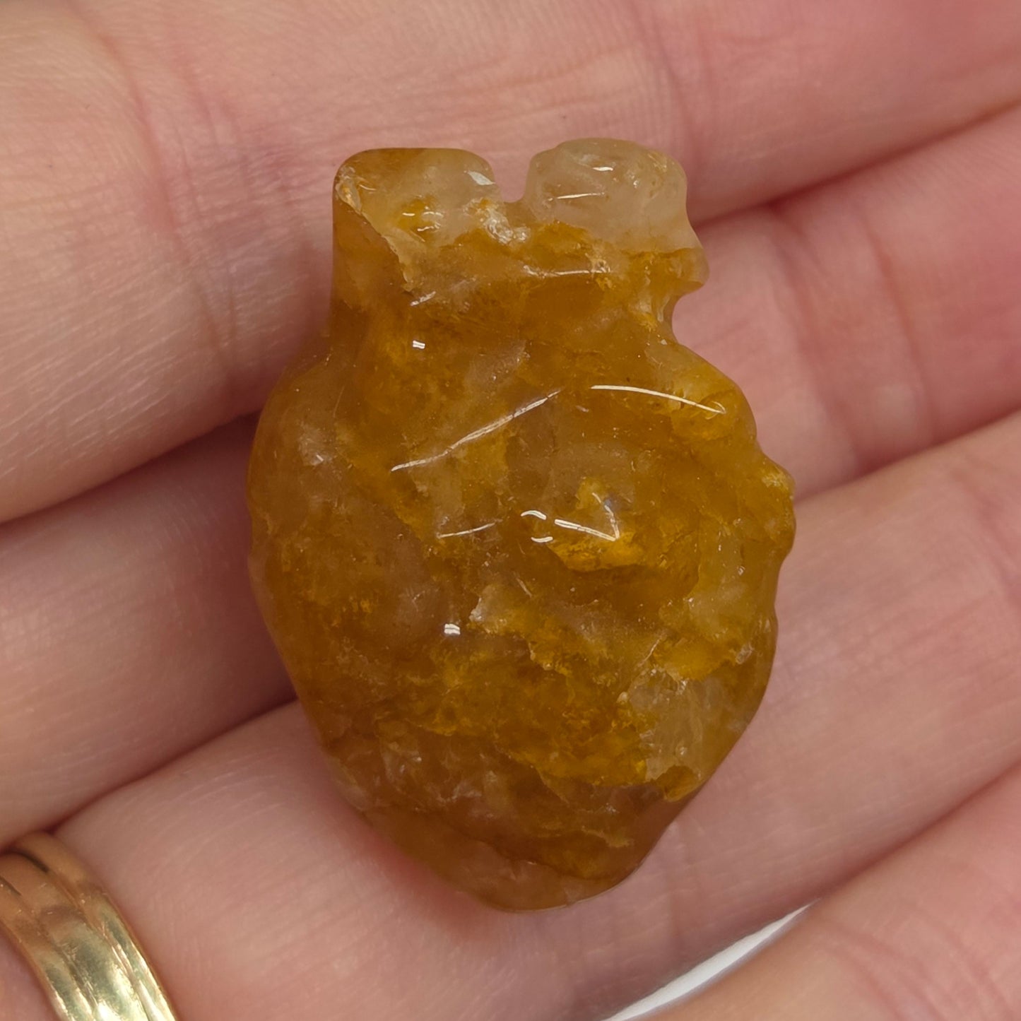 Hand holding a Golden Healer heart shaped carving on a white background