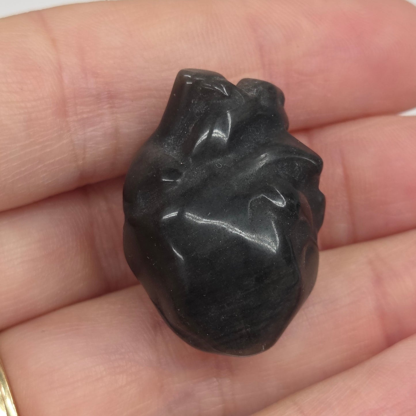 Hand holding an Obsidian heart shaped carving on a white background
