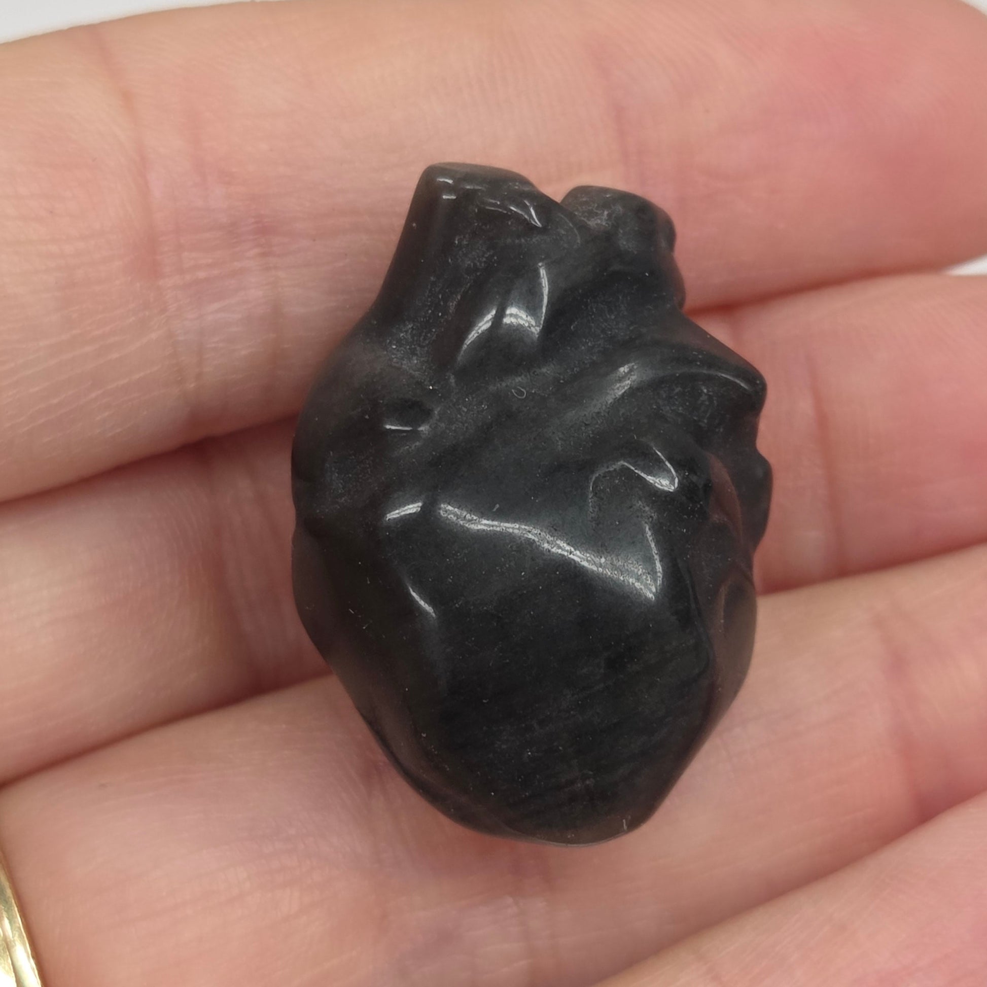 Hand holding an Obsidian heart shaped carving on a white background