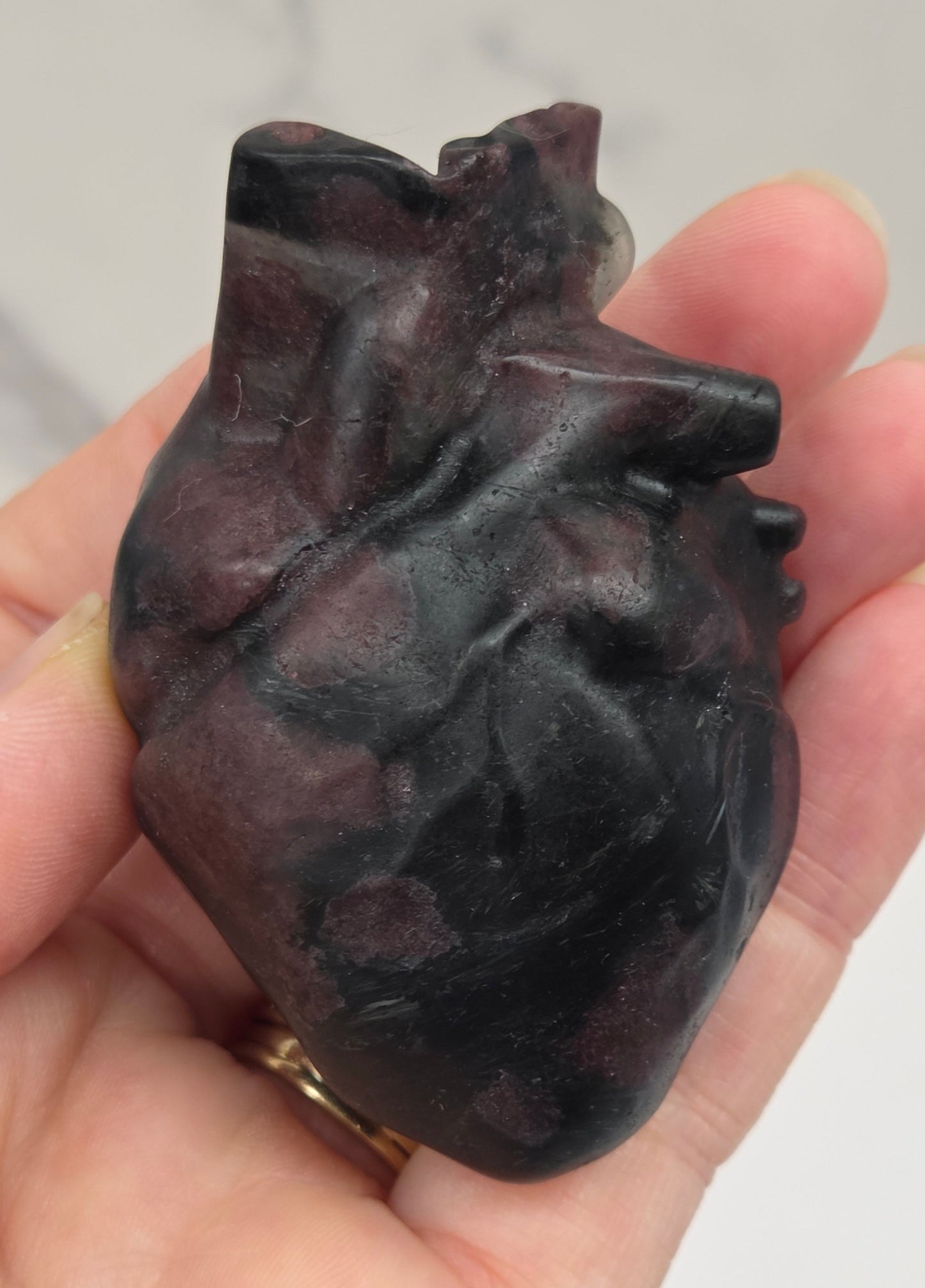 Hand holding a Garnet carving of an anatomical heart against a white background