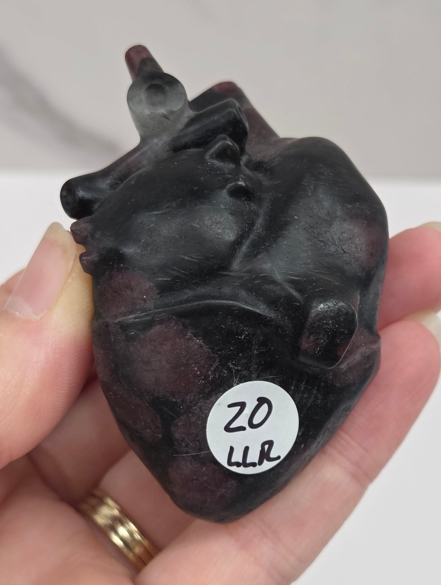 Hand holding a Garnet carving of an anatomical heart against a white background