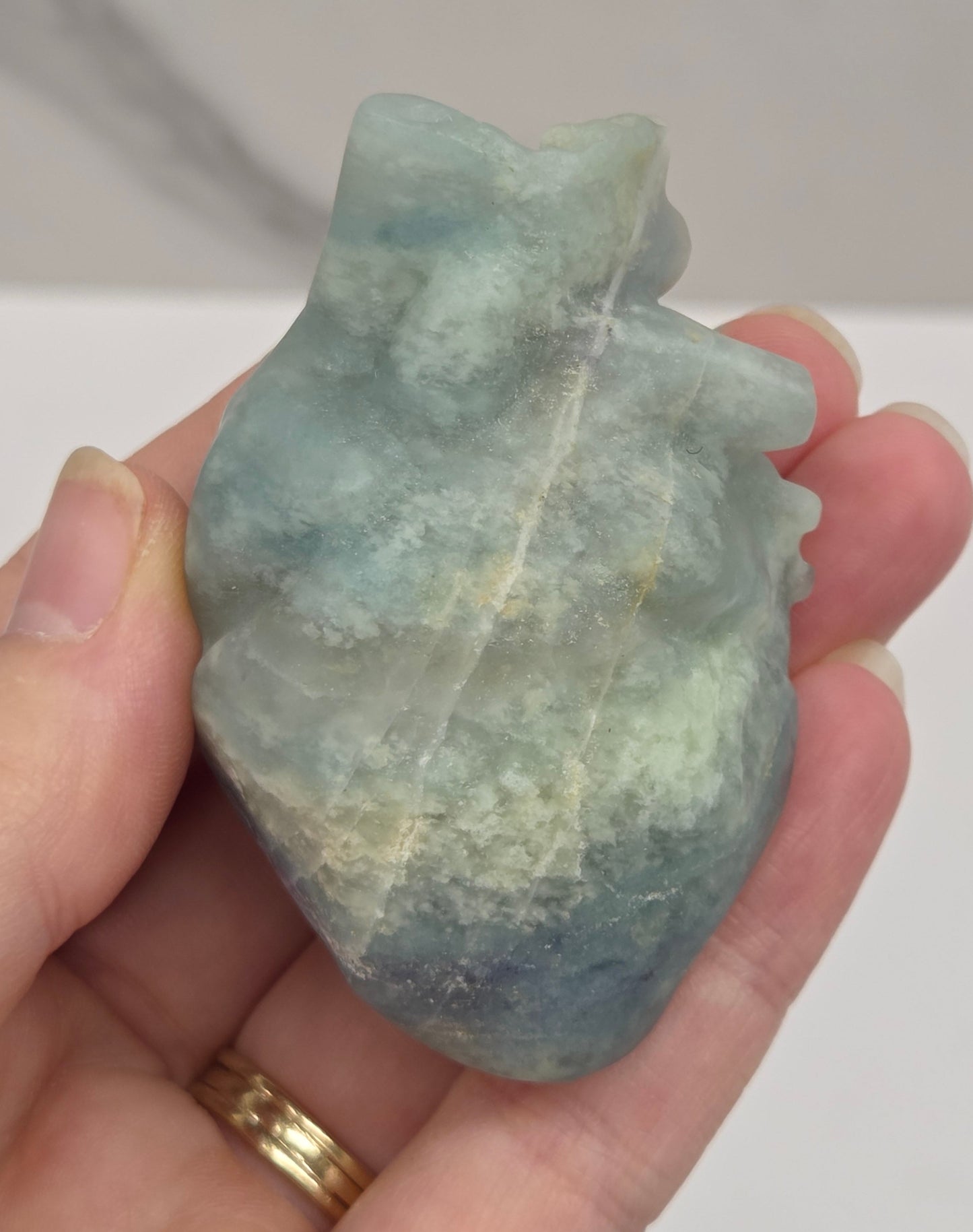 Hand holding a blue calcite carving of an anatomical heart against a white background