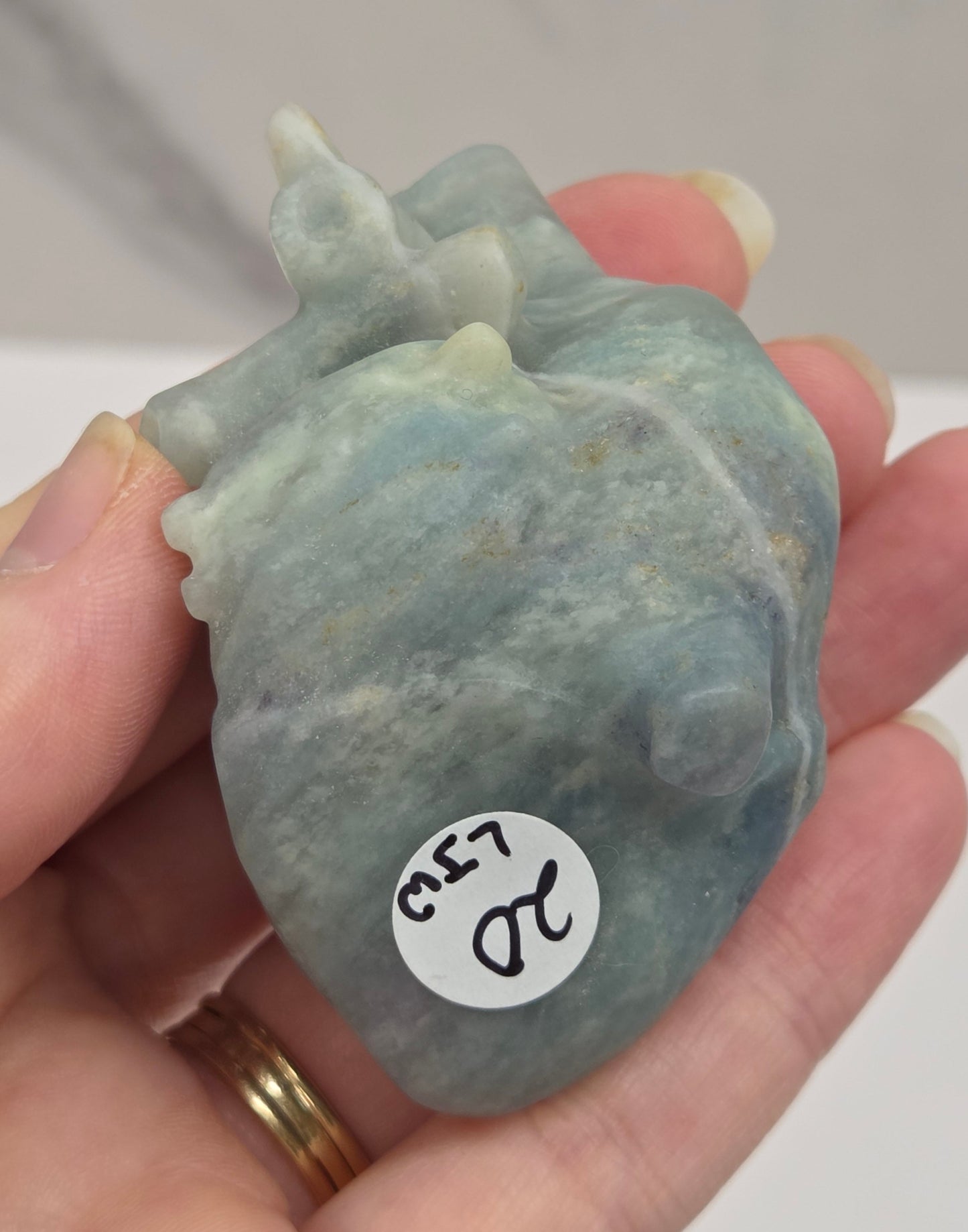Hand holding a blue calcite carving of an anatomical heart against a white background