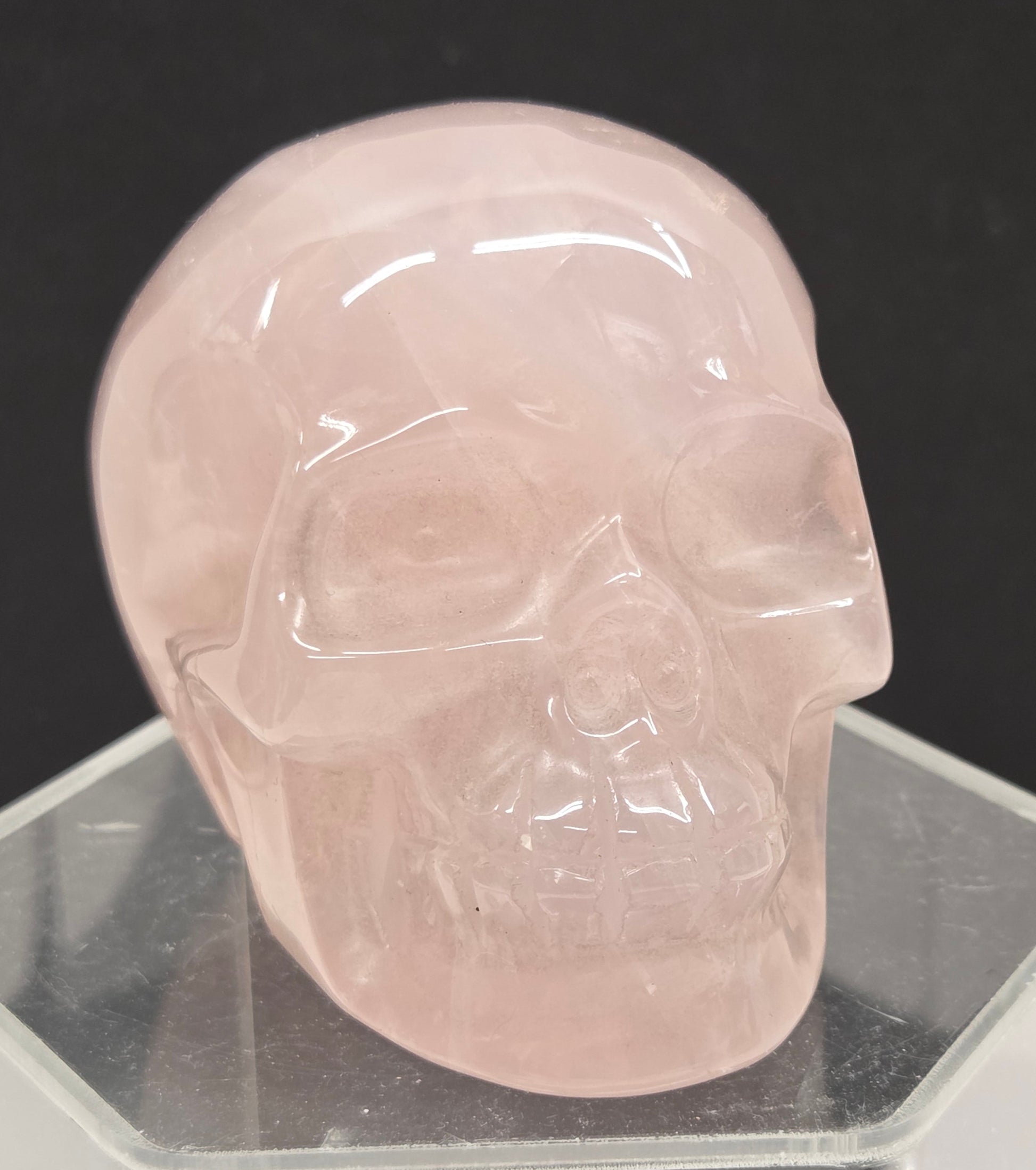 pink rose quartz skull carving on a clear stand against a black background