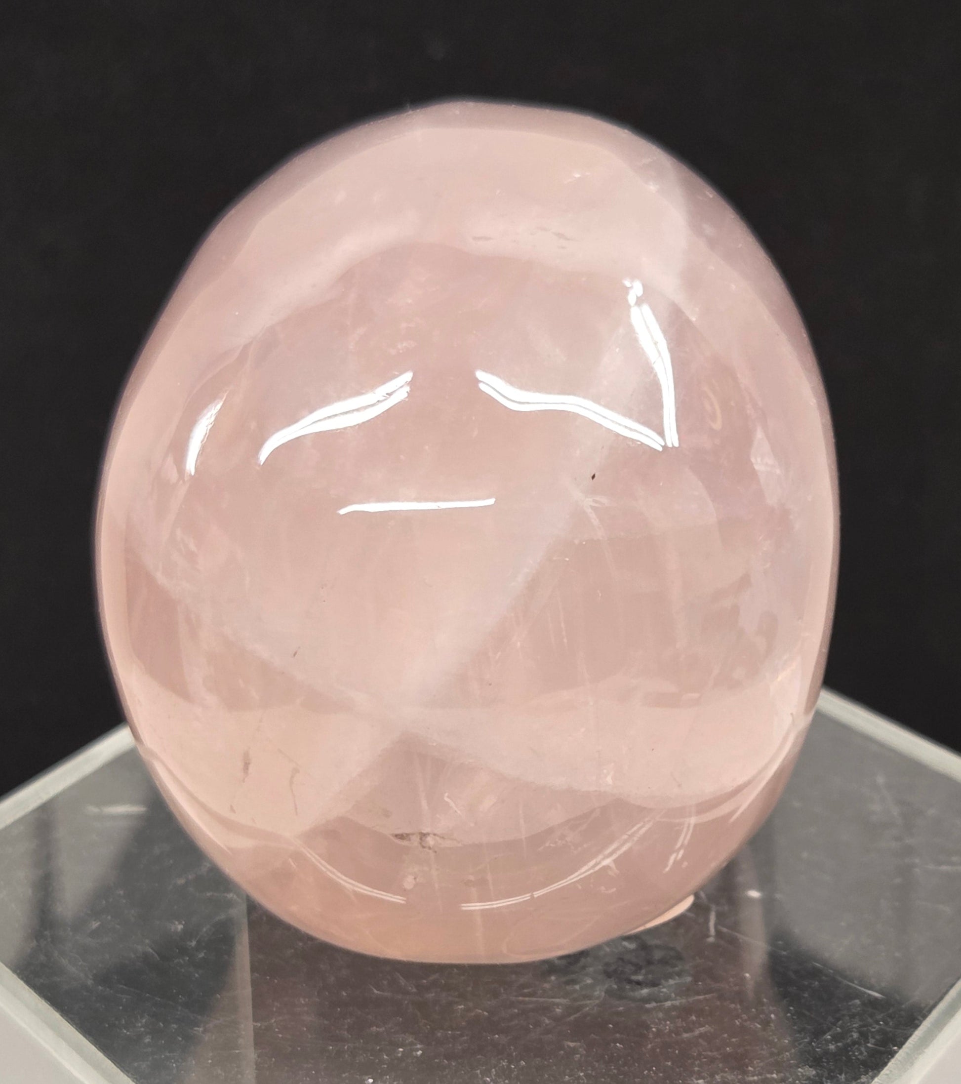 pink rose quartz skull carving on a clear stand against a black background
