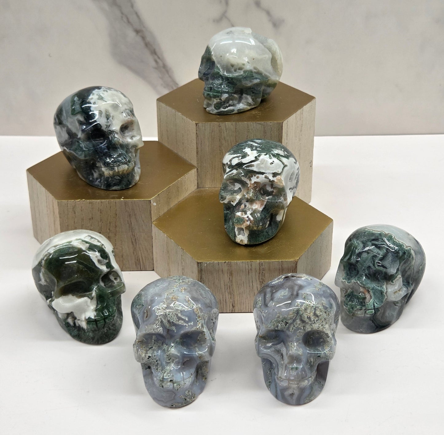 Collection of Moss Agate skull carvings on a wood stand against a white background