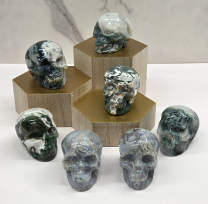 Collection of Moss Agate skull carvings on a wood stand against a white background
