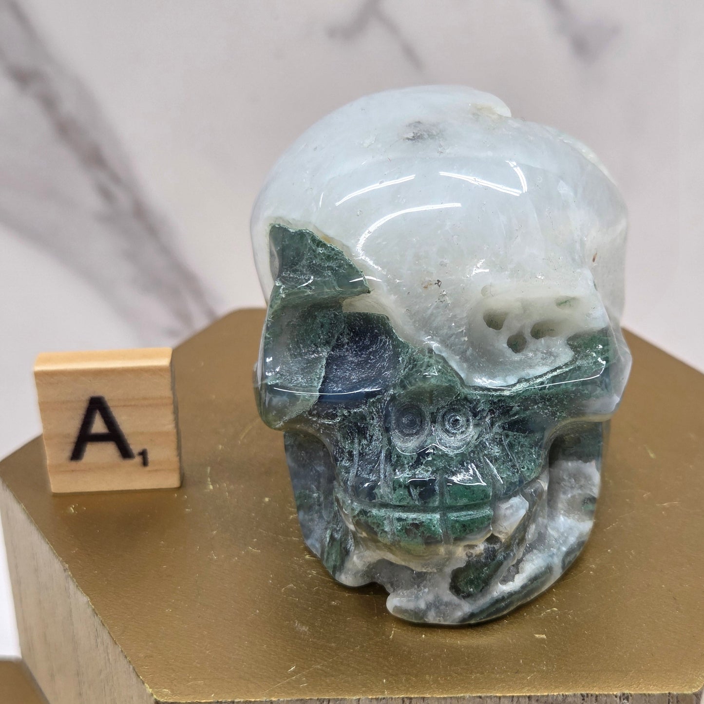 Moss Agate skull carving on a wood stand against a white background