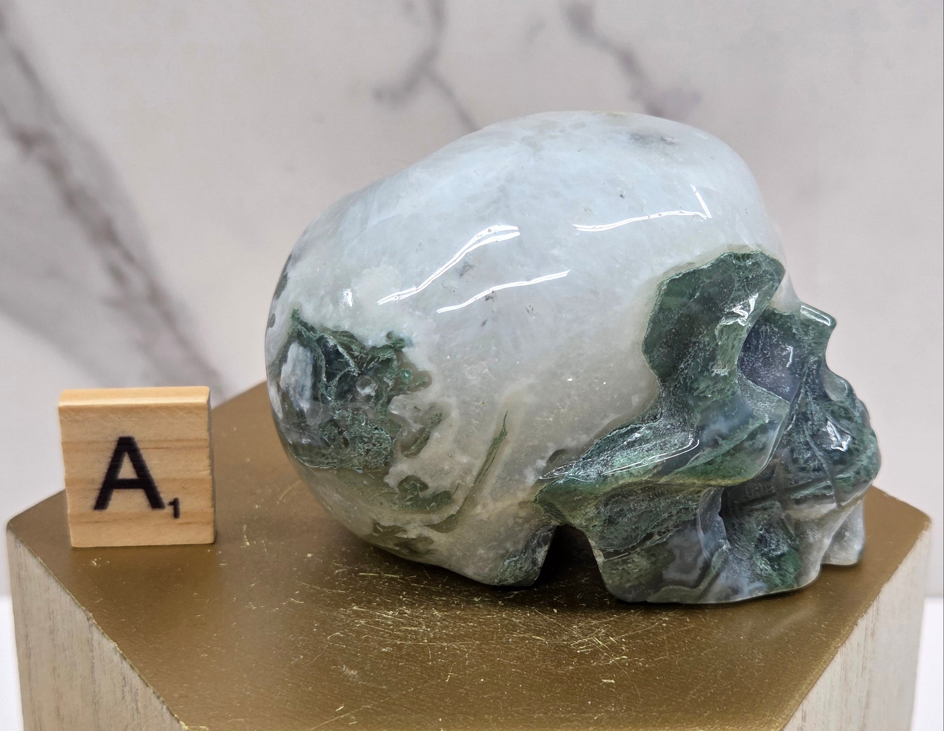 Moss Agate skull carving on a wood stand against a white background