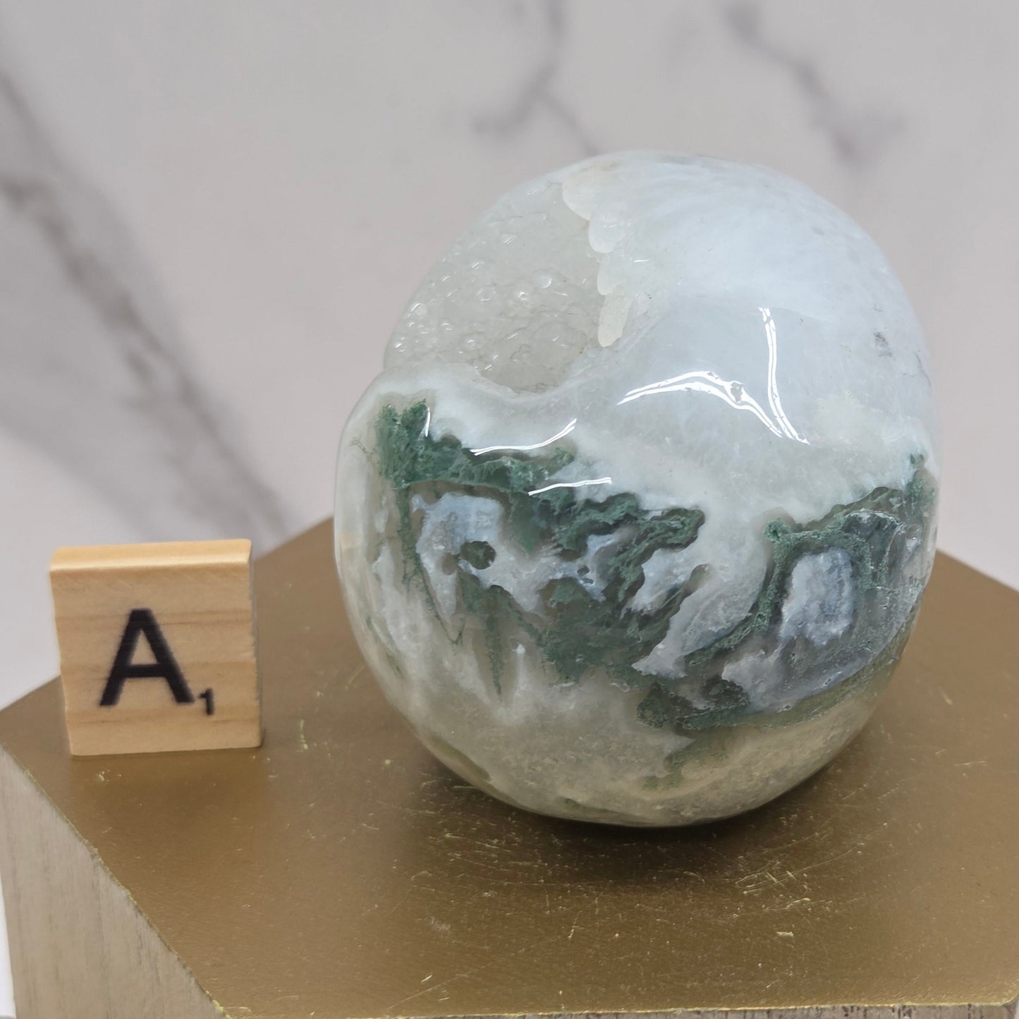 Moss Agate skull carving on a wood stand against a white background