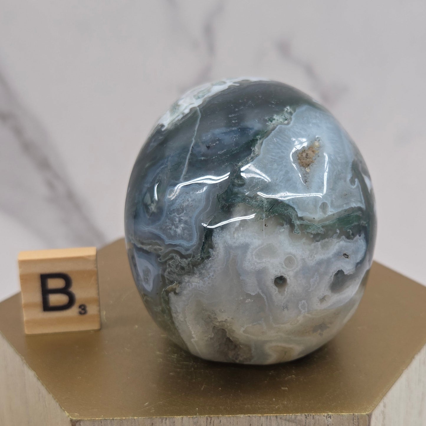 Moss Agate skull carving on a wood stand against a white background
