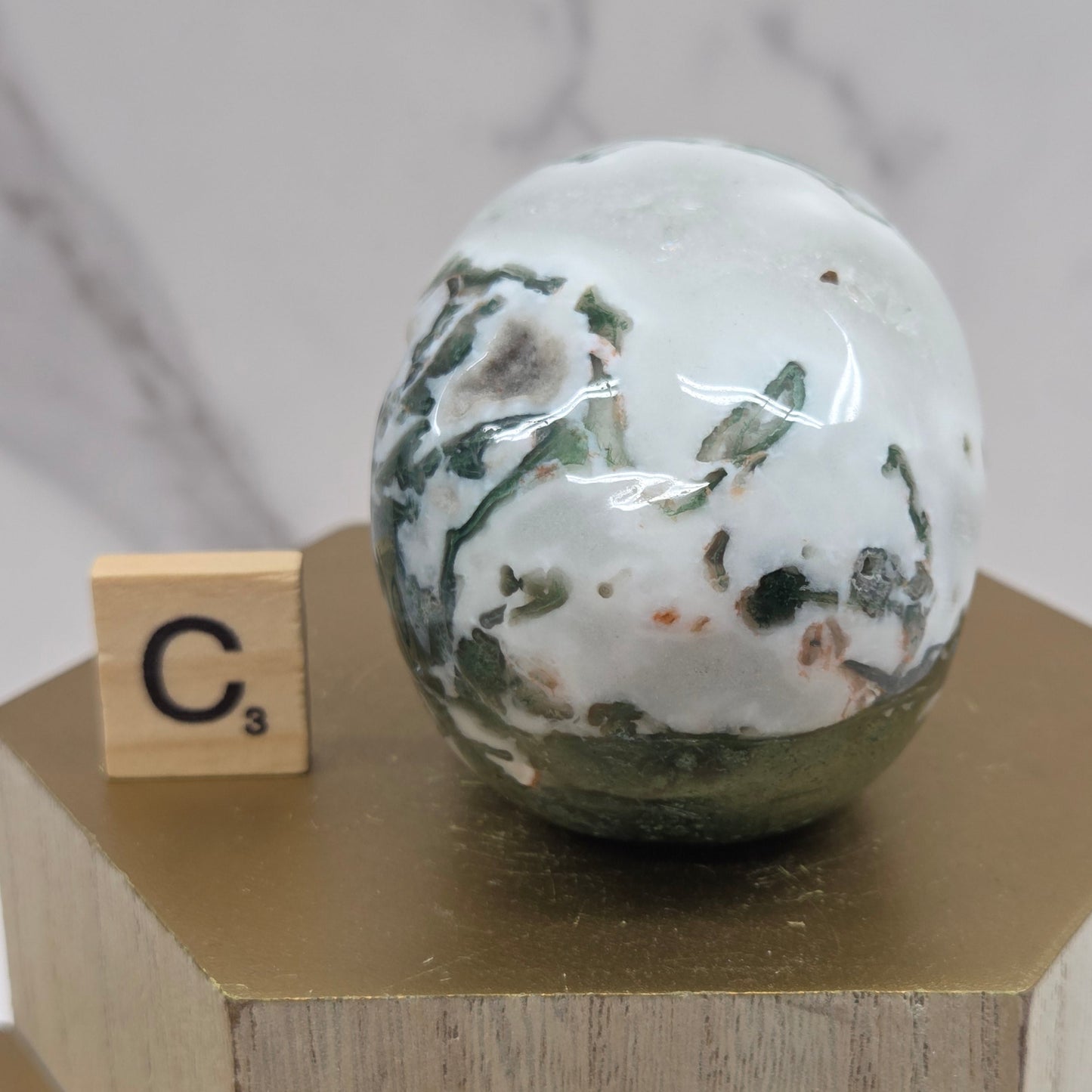 Moss Agate skull carving on a wood stand against a white background