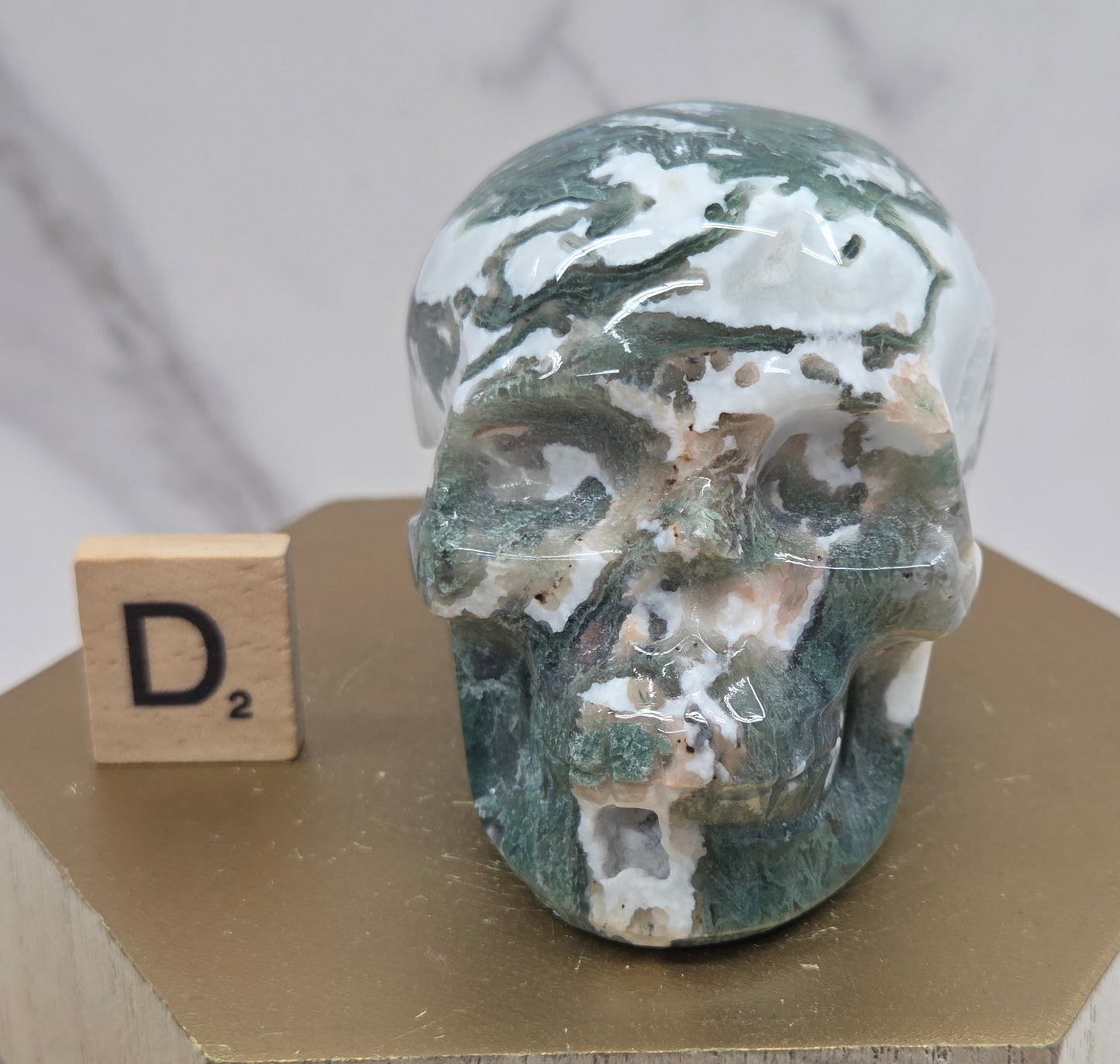 Moss Agate skull carving on a wood stand against a white background