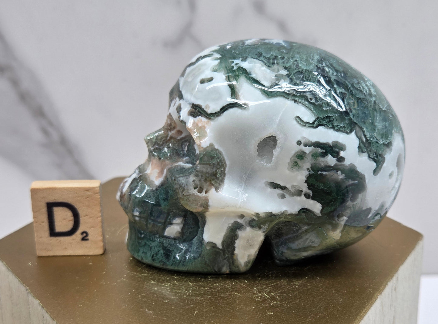 Moss Agate skull carving on a wood stand against a white background