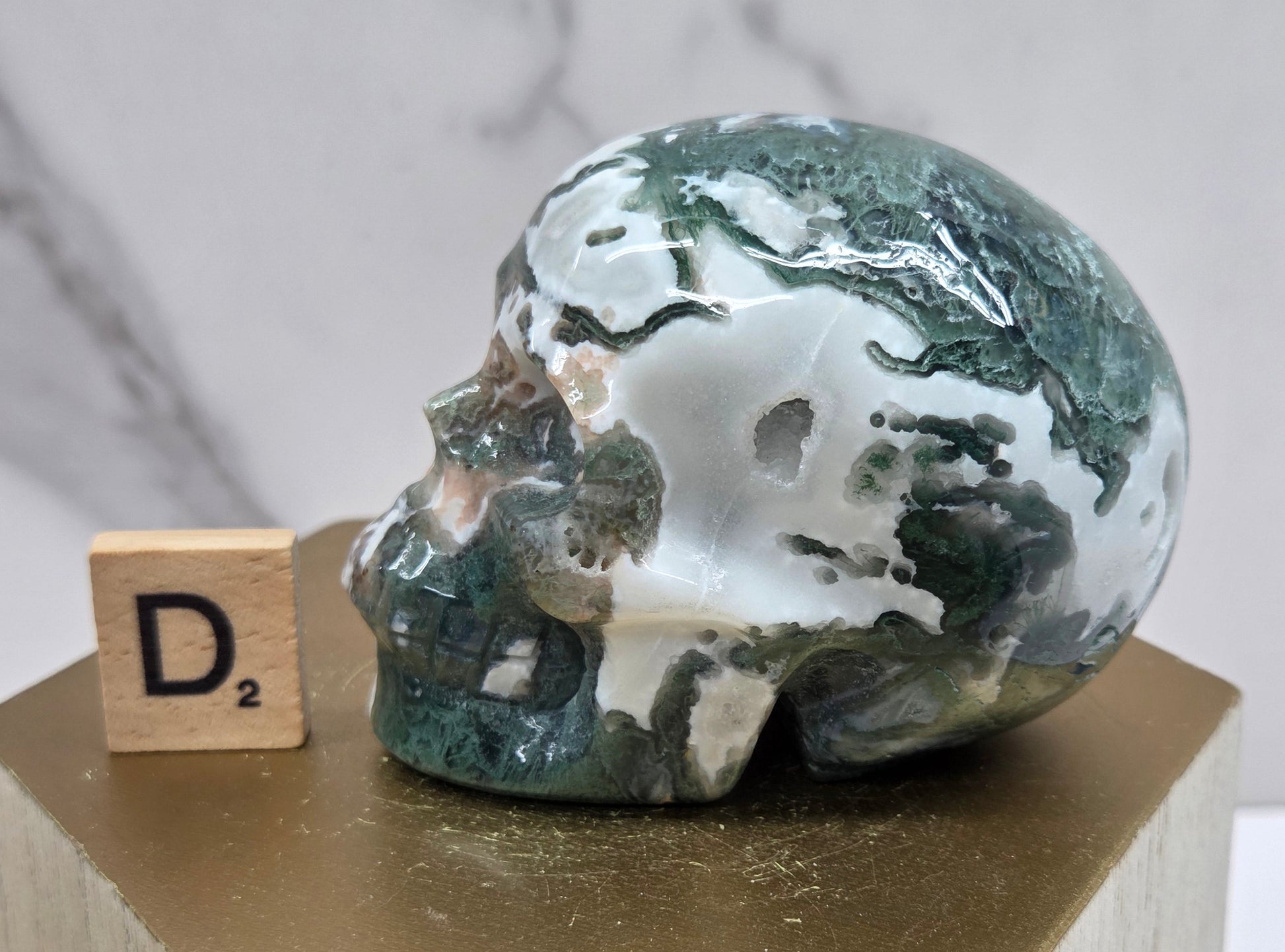 Moss Agate skull carving on a wood stand against a white background