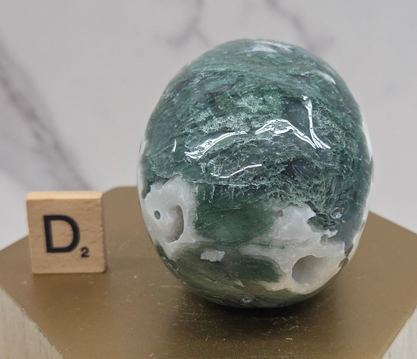 Moss Agate skull carving on a wood stand against a white background