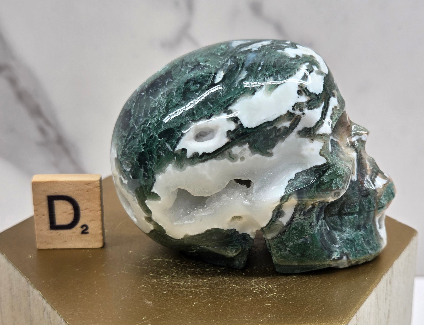 Moss Agate skull carving on a wood stand against a white background