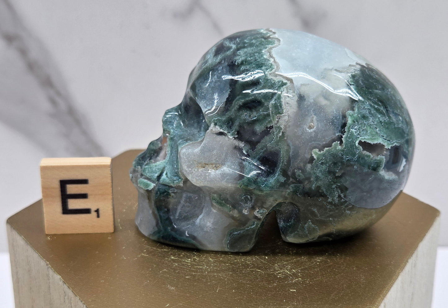 Moss Agate skull carving on a wood stand against a white background