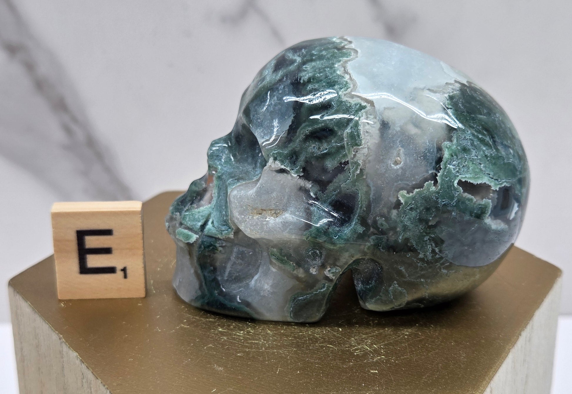 Moss Agate skull carving on a wood stand against a white background
