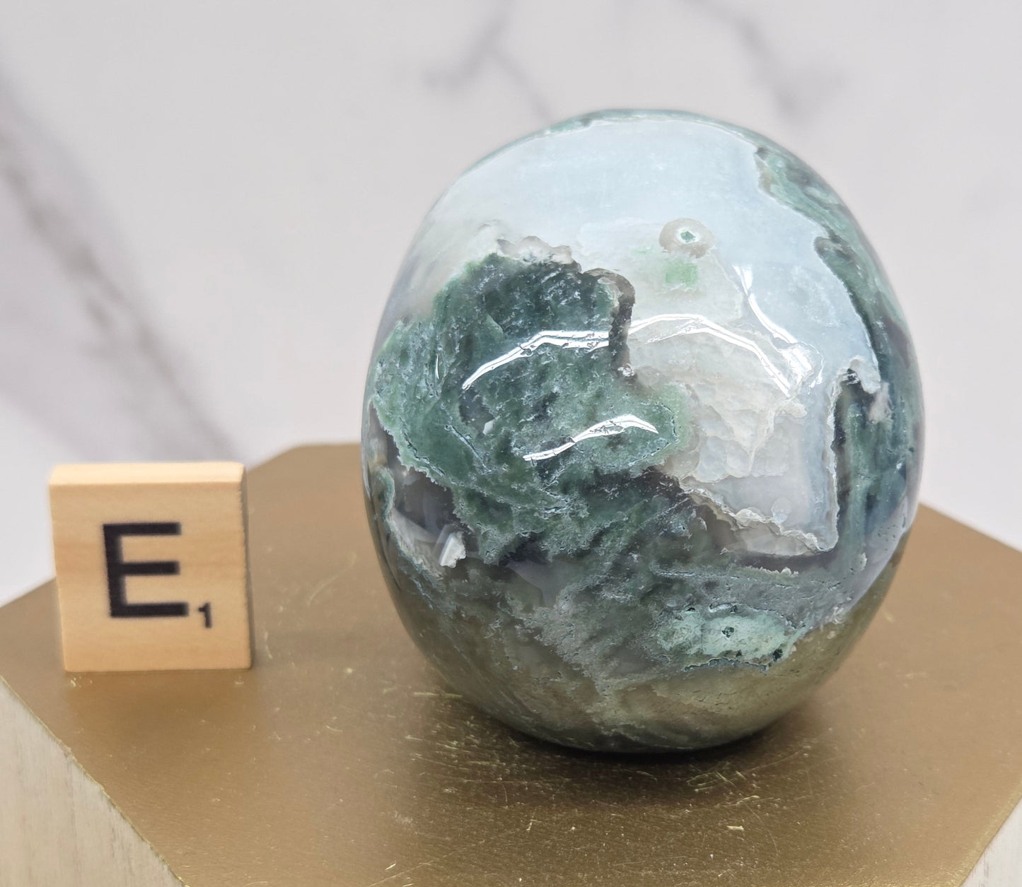 Moss Agate skull carving on a wood stand against a white background