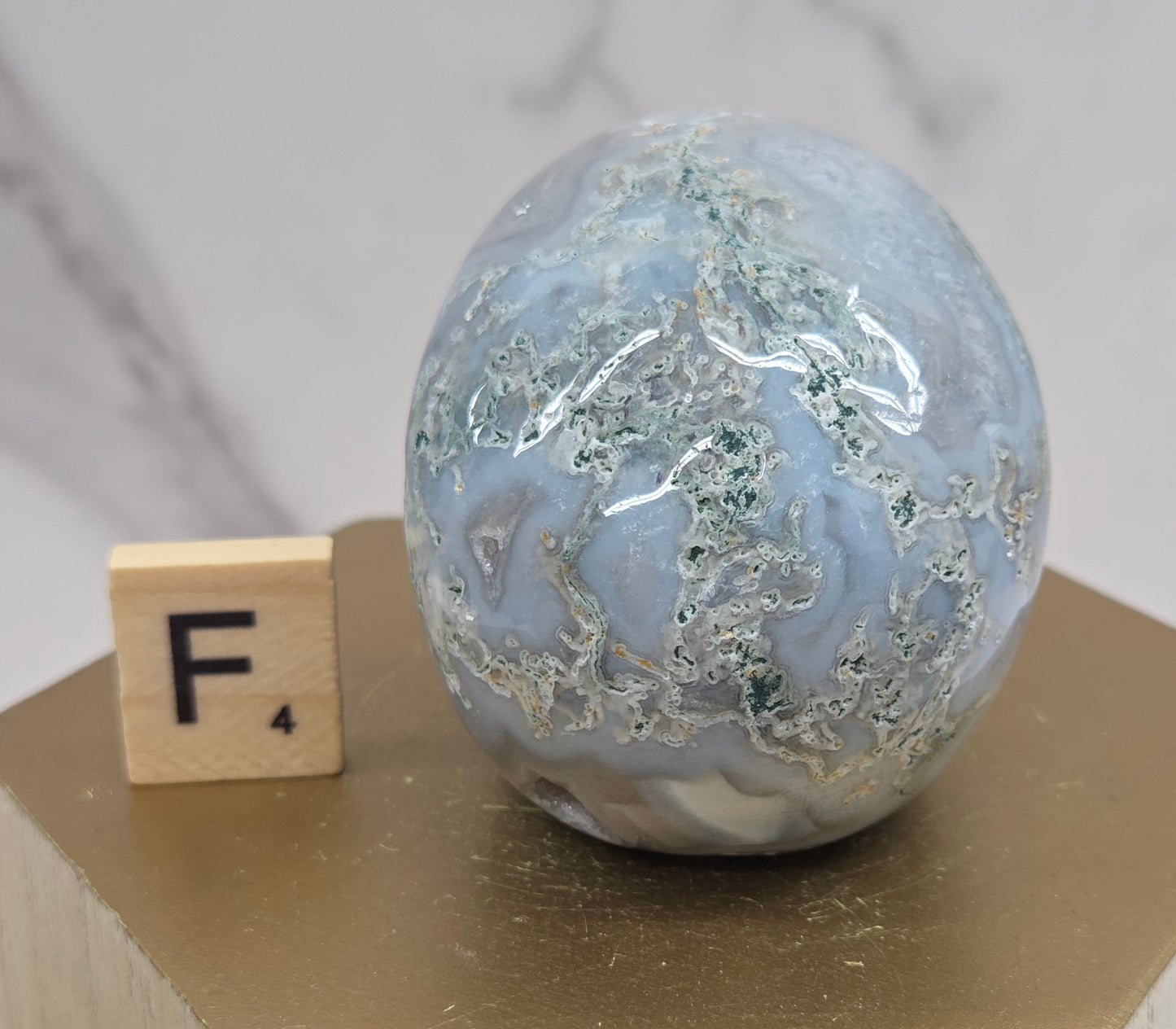 Moss Agate skull carving on a wood stand against a white background