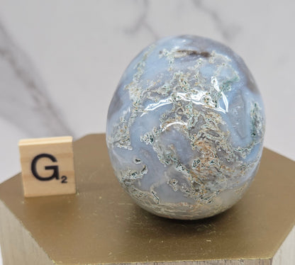 Moss Agate skull carving on a wood stand against a white background