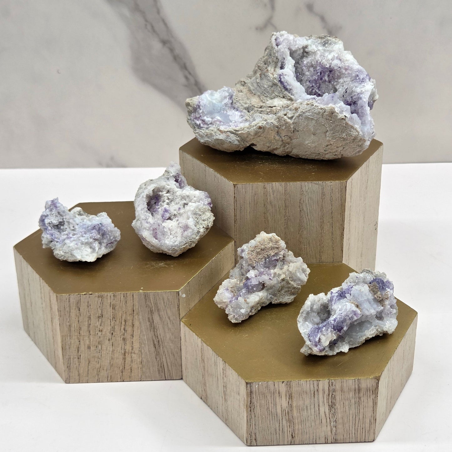 Collection of mineral geodes with white and purple coloring on a wood stand against a white background