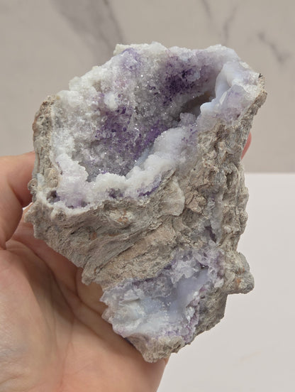 Mineral geode being held in a hand with white and purple coloring against a white background