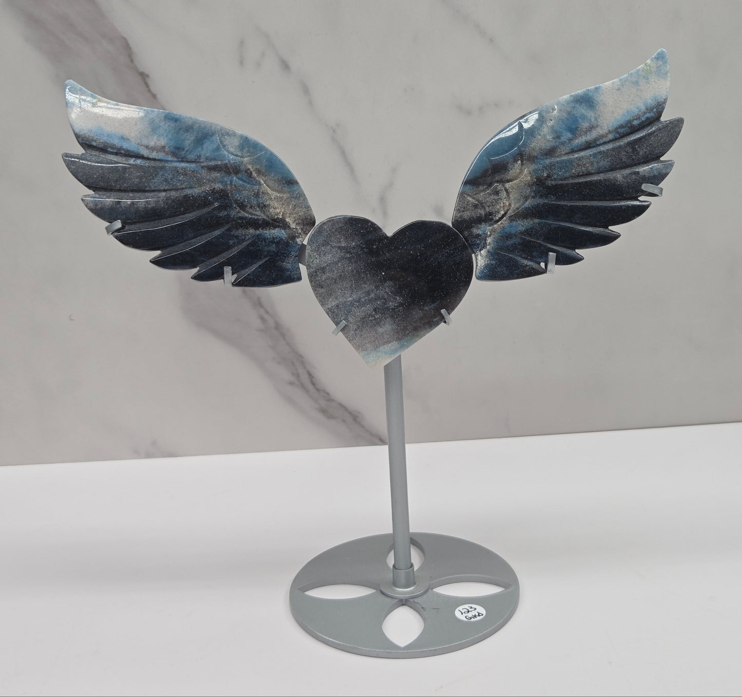 wing and heart carving with black, blue and white coloring on a silver stand against a white background