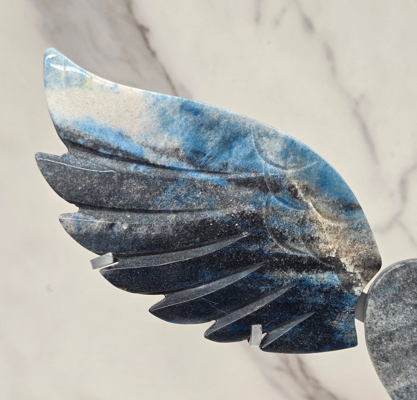 wing and heart carving with black, blue and white coloring on a silver stand against a white background