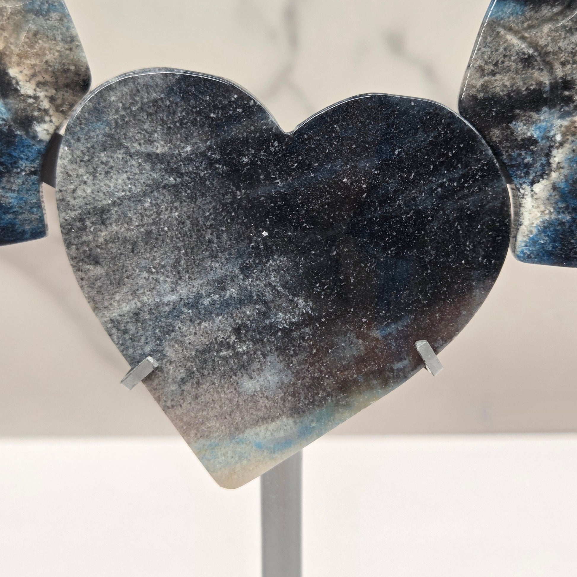 wing and heart carving with black, blue and white coloring on a silver stand against a white background