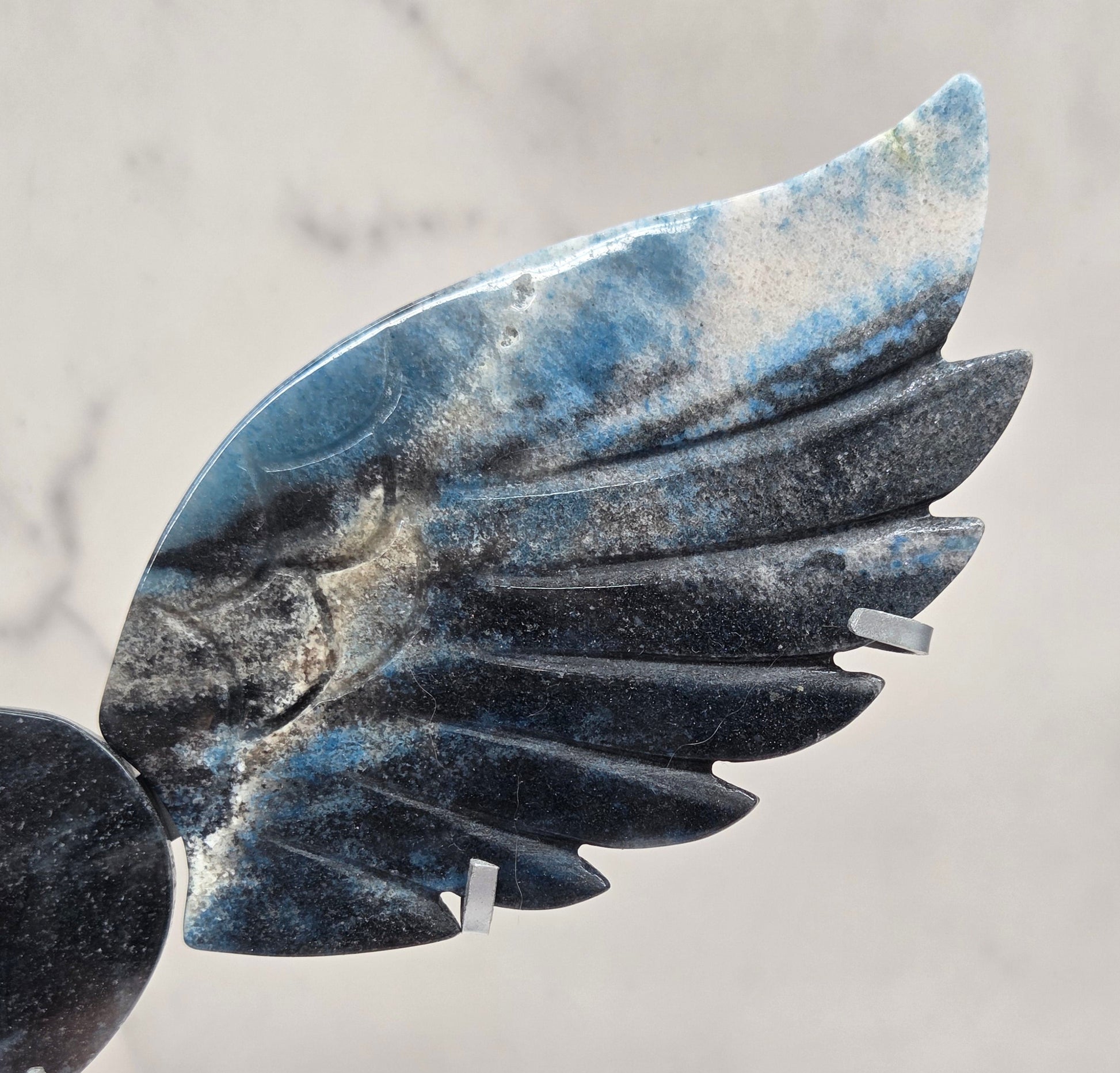 wing and heart carving with black, blue and white coloring on a silver stand against a white background