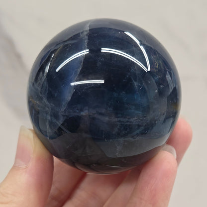 Blue Fluorite sphere being held by a hand against a white background