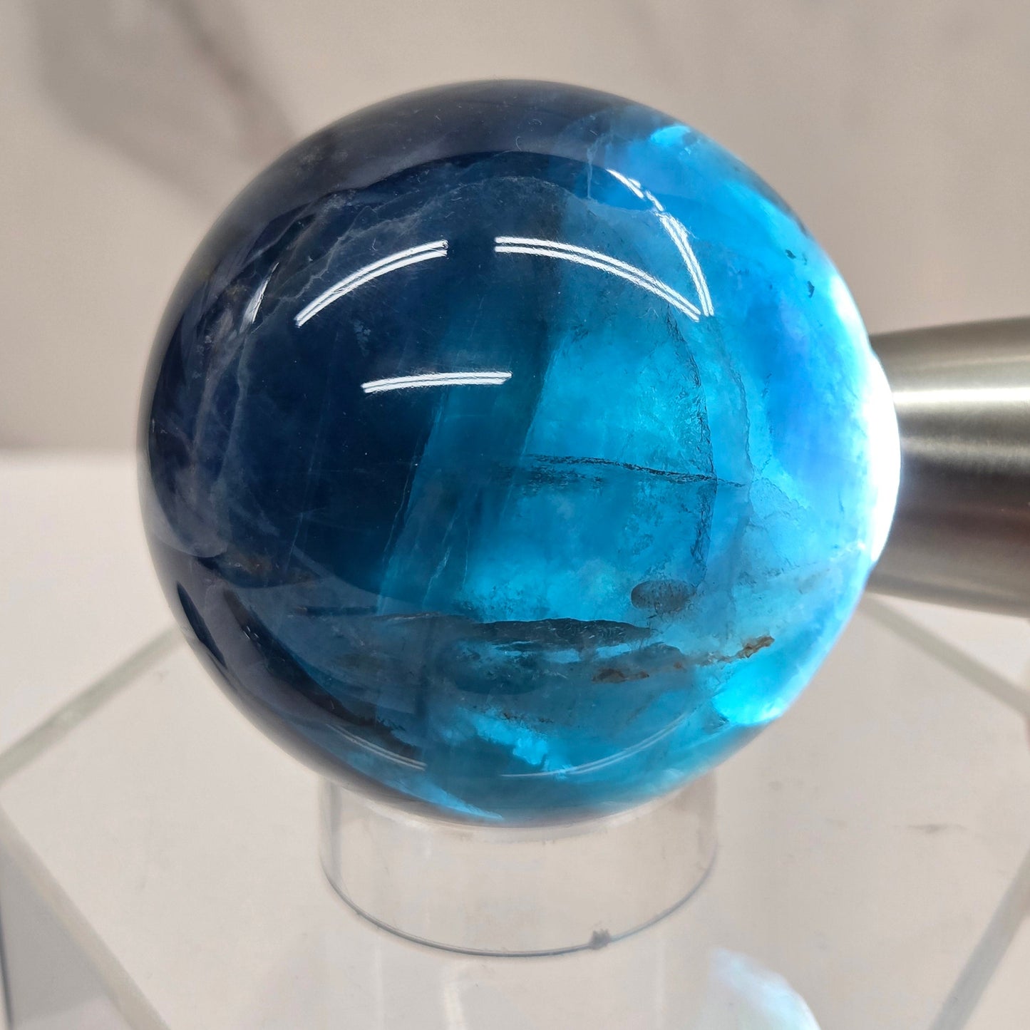 Backlit Blue Fluorite sphere on an acrylic stand against a white background