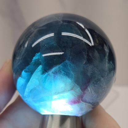 Backlit Blue Fluorite sphere on an acrylic stand against a white background
