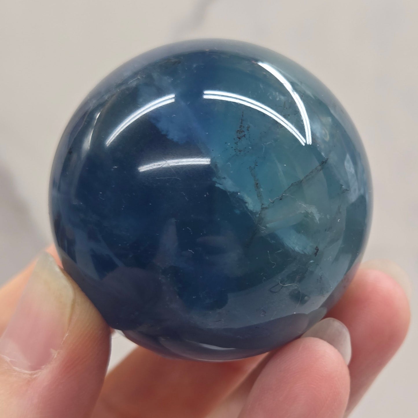 Blue Fluorite sphere being held in a hand against a white background